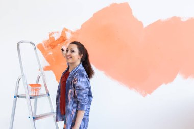 Yeni evin duvarlarını boyayan neşeli bir kadın. Yenileme, onarım ve dekorasyon konsepti. Boşluğu kopyala.