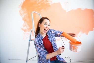 Duvarı boya rulosuyla boyayan komik bir kadın. Yeni dairesinde duvar boyayan güzel bir kadının portresi. Dekorasyon ve yenileme konsepti.