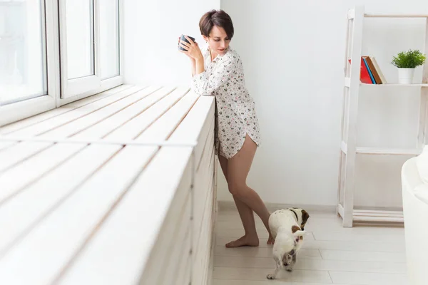Vrouw in gezellig huishemd thuis ontspannen en spelen met hondenboer Russell terrier, thee drinken. Morgenconcept. — Stockfoto