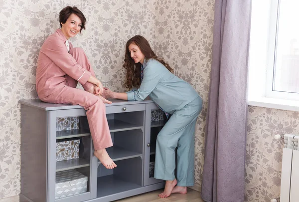 Duas irmãs ou amigos relaxando na sala de estar. Meninas em pijama elegante. Quarentena e ficar em casa conceito. Retrato de comprimento total . — Fotografia de Stock