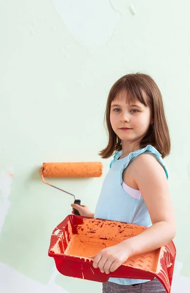 Riparazione nell'appartamento. Ragazza felice dipinge il muro con vernice arancione. Concetto di ristrutturazione e ridecorazione . — Foto Stock