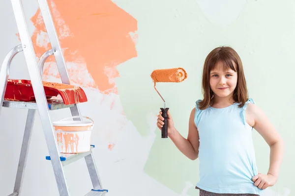 Reparación en el apartamento. La niña feliz pinta la pared con pintura naranja. Concepto de renovación y redecoración . — Foto de Stock