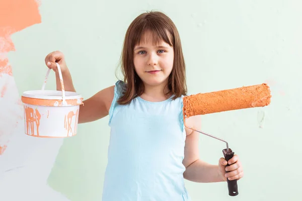 Riparazione nell'appartamento. Ragazza felice dipinge il muro con vernice arancione. Concetto di ristrutturazione e ridecorazione . — Foto Stock