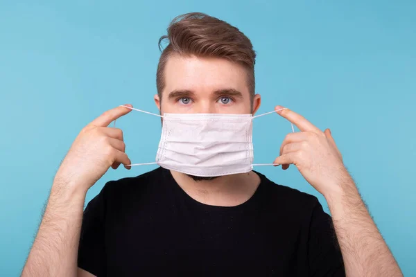 L'homme met un masque médical protecteur en studio bleu pour être à l'abri des virus et des infections. Homme avec masque médical. Coronavirus, covide-19, virus et concept pandémique . — Photo