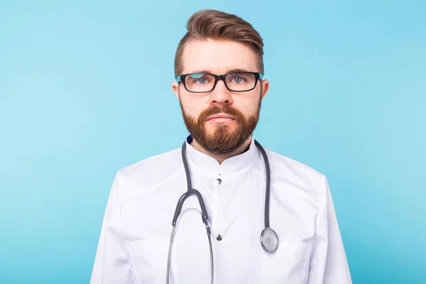 Brodaty lekarz stojący ze stetoskopem na niebieskim tle. Koncepcja medycyny, opieki zdrowotnej i ludzi. — Zdjęcie stockowe