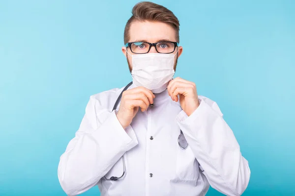 Homme médecin met un masque médical sur fond bleu. Coronavirus, covide-19 et concept de pandémie . — Photo