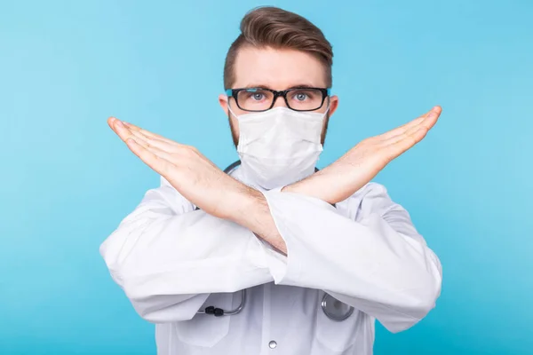 Médecin masculin médical porter un masque pour prévenir le coronavirus 2019 et debout et lever la main pour montrer le symbole de mal isolé sur fond bleu. Concept de prévention des maladies infectieuses. — Photo