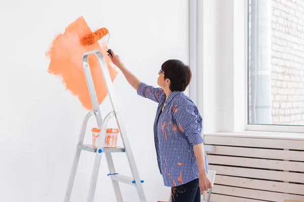 Mujer de mediana edad con rodillo de pintura en el interior. Redecoración, renovación, reparación de apartamentos y concepto de refresco. —  Fotos de Stock