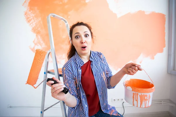 Funny smiling woman painting interior wall of home with paint roller. Redecoration, renovation, apartment repair and refreshment concept. — Stock Photo, Image