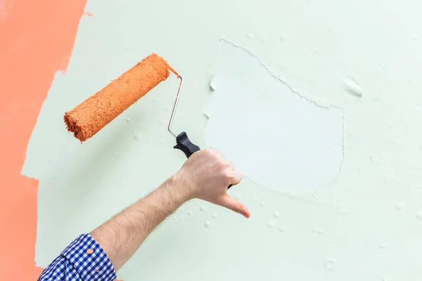 Rullo di vernice mano maschile immerso nel colore arancione e mostrando il pollice verso il basso contro la parete verde. Copia spazio . — Foto Stock