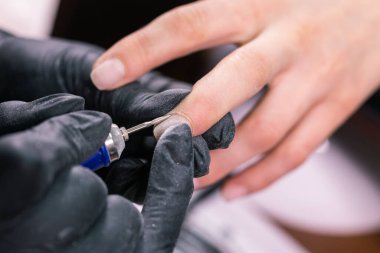 Güzellik salonunda hırdavatçı manikürü. Kadın manikürcü kadın parmaklarına manikür yapmak için elektrikli tırnak matkabı uyguluyor. Mekanik manikür yakın plan. Vücut bakımını kabul et.