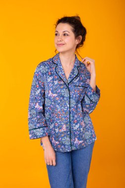 Mavi elbiseli, gülümseyen ve eğlenen heyecanlı genç bir kadın. Sarı arkaplanda izole edilmiş.