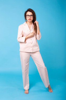 Mavi arka planda pijamalarıyla poz veren genç bir kız. Rahatla iyi ruh hali, yaşam tarzı ve uyku kıyafetleri konsepti.