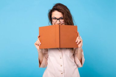 Genç kız mavi arka planda pijamalarıyla kitap okuyor. Rahatla iyi ruh hali, yaşam tarzı ve uyku kıyafetleri konsepti.