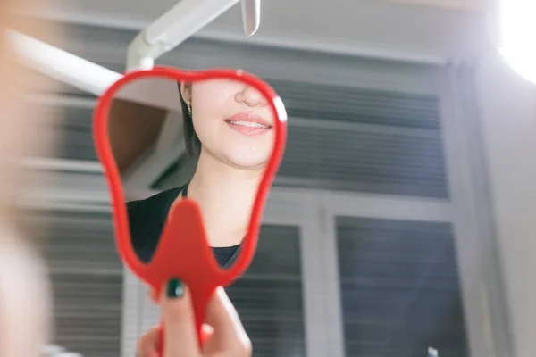 Жінка перевіряє зуби у дзеркалі. Усміхнена жінка в стоматологічному кабінеті. Посміхайся ширше і будь красивим . — стокове фото
