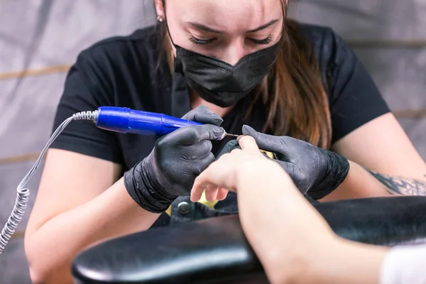 Manicurist use electric nail file drill in beauty salon. Perfect nails manicure process close up with burst flying debris. — Stock Photo, Image