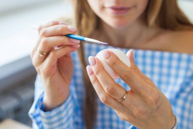 Tatiller, el yapımı ve yaratılış konsepti - Mutlu genç kadın Paskalya yumurtasına yakın plan çiziyor..