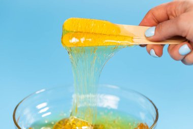 Eksiltme ve güzellik kavramı - saç için şeker macunu ya da bal mumu parlak mavi arkaplan üzerinde ahşap çerçeve çubukları ile spatulayı kaldırmak