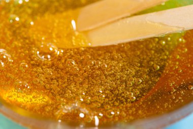 Depilasyon ve güzellik konsepti - parlak mavi arkaplan üzerinde ahşap çerçeve çubukları ile spatulayı kaldırmak için şeker macunu veya bal mumu yakın plan. Makro fotoğrafçılık.