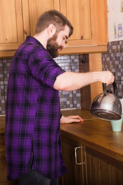 Sakallı adam ev mutfağında kahvaltıda çay yapıyor. Sabah ve kahvaltı konsepti.