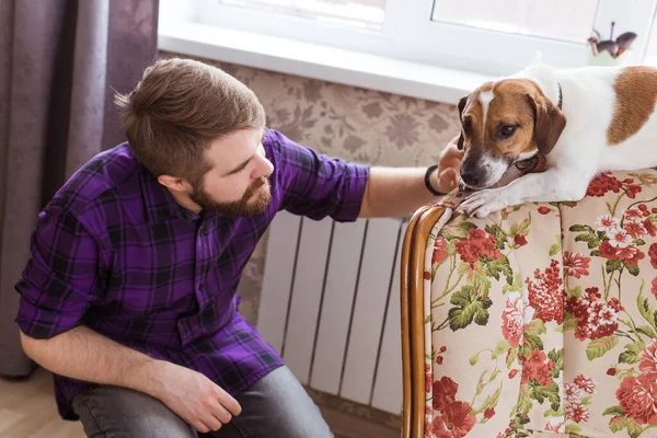 Joyeux jeune homme assis avec son chien à la maison. Propriétaire d'animal, animaux et concept d'amitié . — Photo