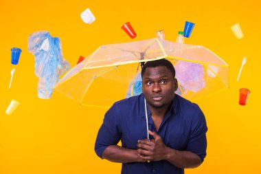 Çöp, plastik geri dönüşüm, kirlilik ve çevre konsepti sorunu - sarı arka planda çöplü dalgın Afrikalı Amerikalı adam.