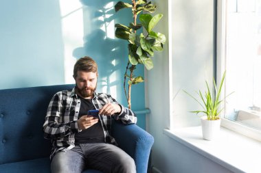 Evdeki kanepede oturmuş akıllı bir telefonla online oyunlar oynayan bir adam..