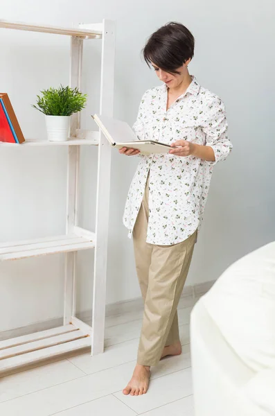 Bella giovane donna in piedi vicino alla finestra a leggere un libro . — Foto Stock