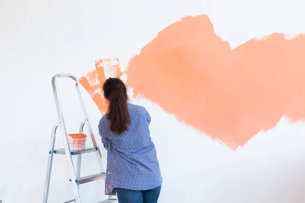 Happy young woman painting interior wall with paint roller in new house. A woman with roller applying paint on a wall. Copy space.