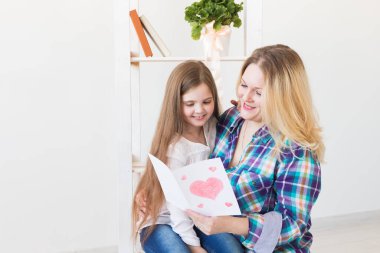 Anneler Günün kutlu olsun. Çocuk kızı annesini tebrik eder ve ona kartpostal verir. Anne ve kız gülümsüyor ve sarılıyorlar. Aile tatili ve annelik.