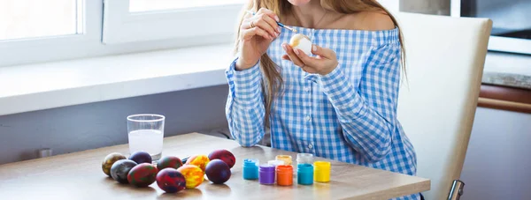 Holidays, handmade and creation concept - Happy young woman draws on Easter egg, close-up.