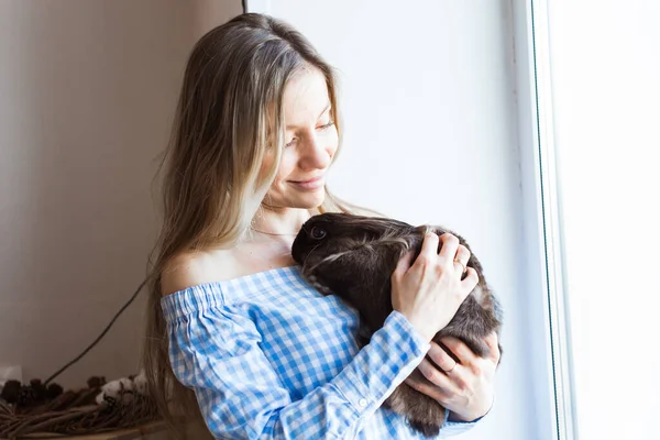 Pet och påsk koncept - Attraktiv flicka kramar brun kanin hemma, närbild. — Stockfoto