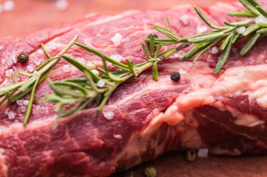 Ahşap arka planda baharatlı ve otlu biftekli çiğ biftek, yakın plan..