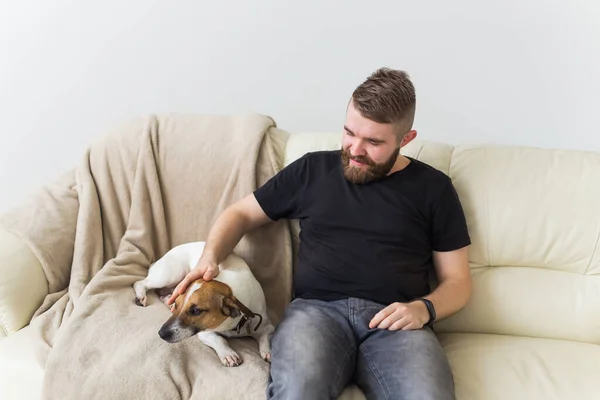 Attractive cheerful Caucasian male in casual t shirt sitting on couch favourite pet. Happy bearded man with his jack russell terrier. Pets owner concept. — Stock Photo, Image
