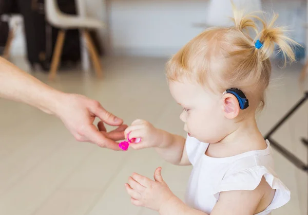 Hearing aid in baby girls ear. Toddler child wearing a hearing aid at home. Disabled child, disability and deafness concept.