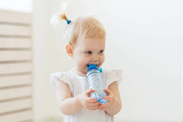 Liten småbarn flicka med flaska mineralvatten hemma. Barn- och familjebegreppet. — Stockfoto