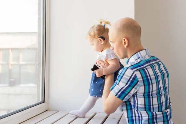 Hearing aid in baby girls ear. Toddler child wearing a hearing aid at home. Disabled child, disability and deafness concept.