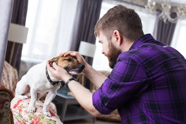 Feliz joven sentado con su perro en casa. Propietario de mascotas, animales y concepto de amistad . — Foto de Stock