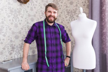 Erkek terzi, terzi, stil sahibi erkek model elbise tasarımcısı. Boyunda bant var. Yaratıcı kıyafet tasarım stüdyosundaki mankenin yanında duruyor..