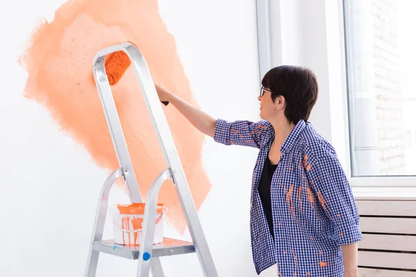 Happy middle-aged woman painting wall in her new apartment. Renovation, redecoration and repair concept.