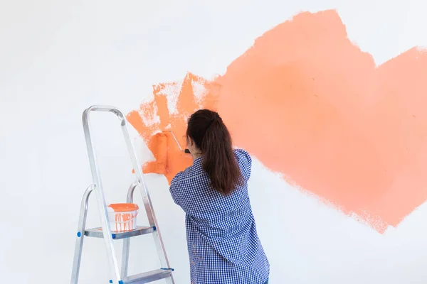 O femeie destul de zâmbitoare pictând peretele interior al casei cu role de vopsea. Redecorare, renovare, reparații apartamente și concept de băuturi răcoritoare. Copiați spațiul . — Fotografie, imagine de stoc