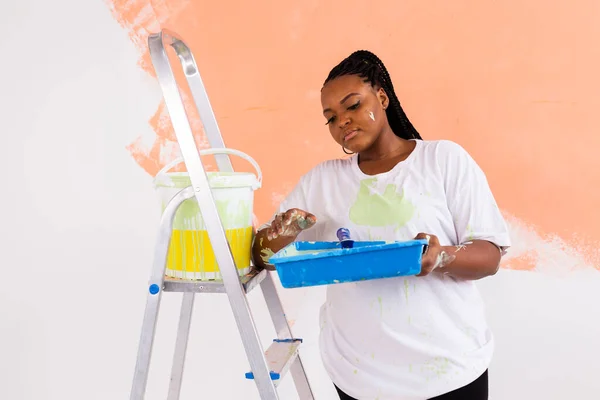 Afro kadın yeni evin duvarlarını boyuyor. Yenileme, onarım ve yeniden dekorasyon konsepti. — Stok fotoğraf