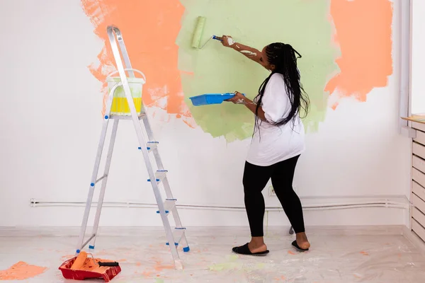 Felice donna afroamericana pittura muro nel suo nuovo appartamento. Concetto di ristrutturazione, ridecorazione e riparazione. — Foto Stock