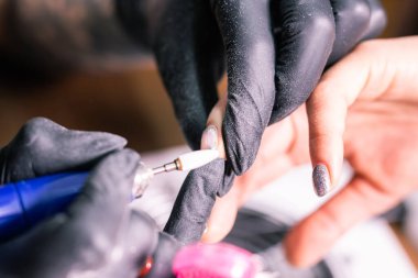 Manikürcü kadının yakın çekimi, manikür makinesi kullanarak müşterilerin tırnaklarındaki jöle parlatmasını kaldırıyor. Manikür ustası güzellik salonunda elektrikli tırnak matkabıyla çalışıyor. Donanım manikür süreci.