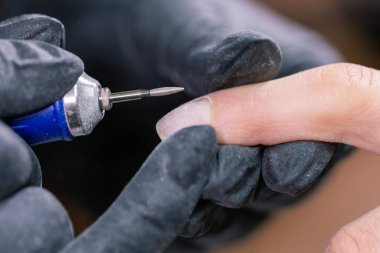 Kadın güzellik salonunda elektrikli tırnak matkabı kullanıyor. Manikür işlemini detaylıca yapıyor. Jel cilası yakın çekim konsepti.