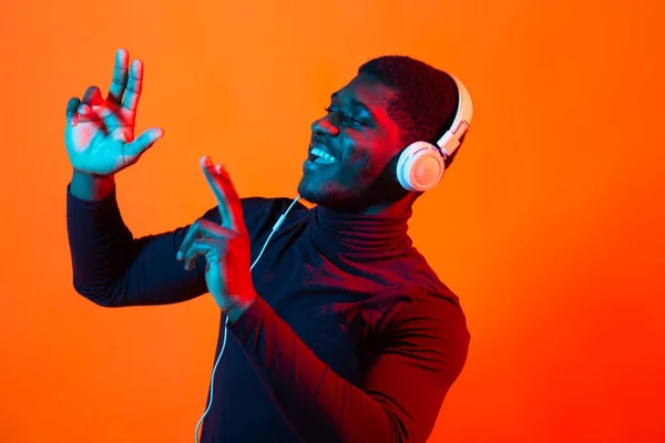 Αφροαμερικάνος νεαρός που ακούει μουσική στο διαδίκτυο χορεύοντας και τραγουδώντας με ακουστικά, νέον φως. Μουσική και τεχνολογία. — Φωτογραφία Αρχείου
