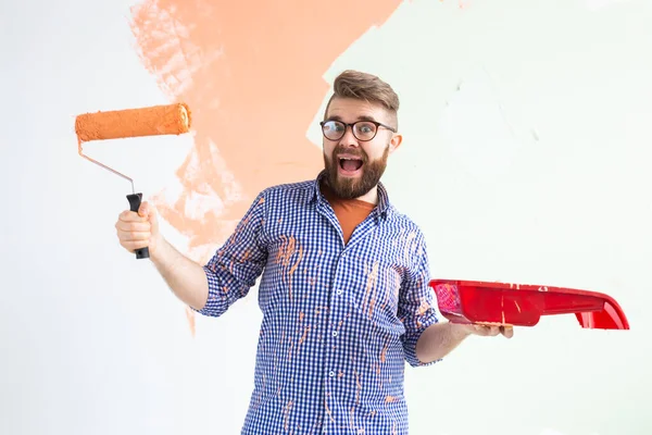 Funny man painting interior wall with paint roller in new house. Guy with roller applying paint on a wall. — Stock Photo, Image