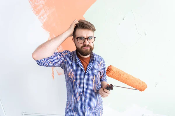 Funny confused man painting the walls of new home. Renovation, repair and redecoration concept. — Stock Photo, Image