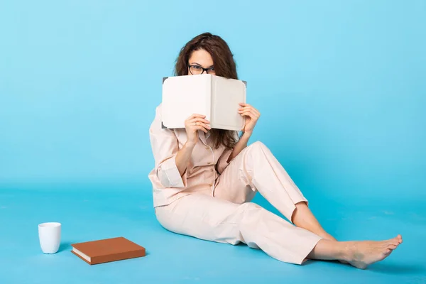 Giovane ragazza in posa con libri in pigiama su sfondo blu. Rilassati buon umore, stile di vita e concetto di pigiama party . — Foto Stock