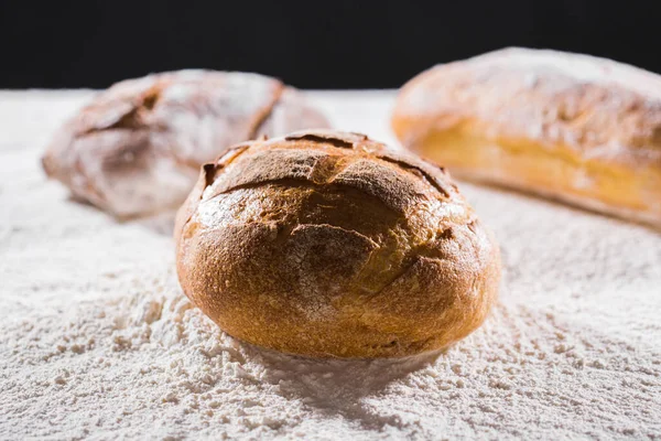 Färskt bröd på bordet närbild i mjöl placer. Färskt bröd på köksbordet. Hälsosam kost och traditionellt bageri koncept. Rustik stil. — Stockfoto